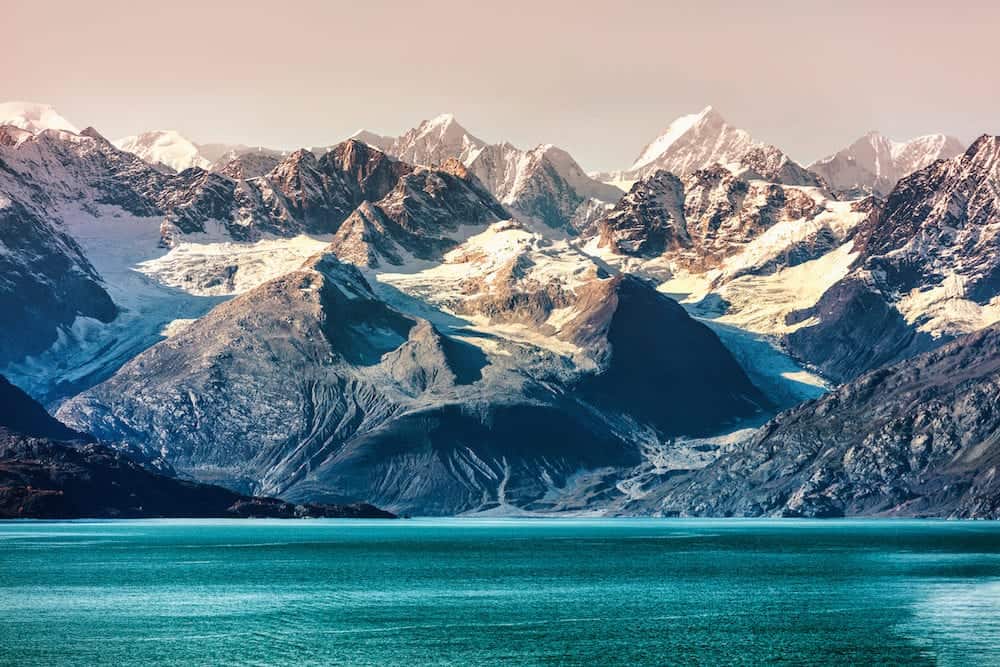 Glacier Bay National Park, Alaska, USA. Alaska cruise travel view of snow capped mountains at sunset. Amazing glacial landscape view from cruiseship vacation showing snowy mountain peaks.