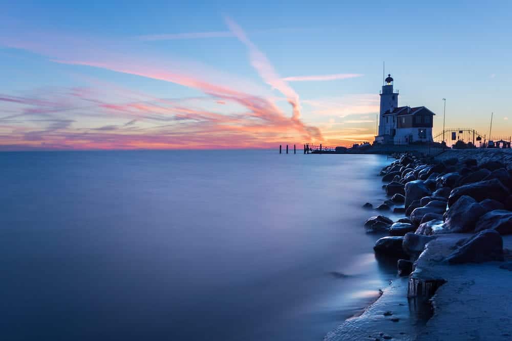 The lighthouse Paard van Marken on Marken island near Volendam and Amsterdam on a cold morning with ice on the rocks that form the pier into IJsselmeer lake at sunrise during the Blue Hour in the Netherlands.