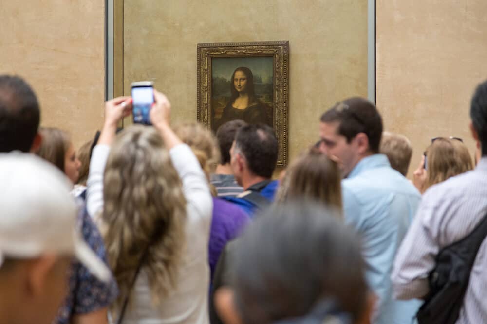 Paris, France - Group of people looking at the famous Mona Lisa painting by artist Leonardo da Vinci inside the Louvre Museum