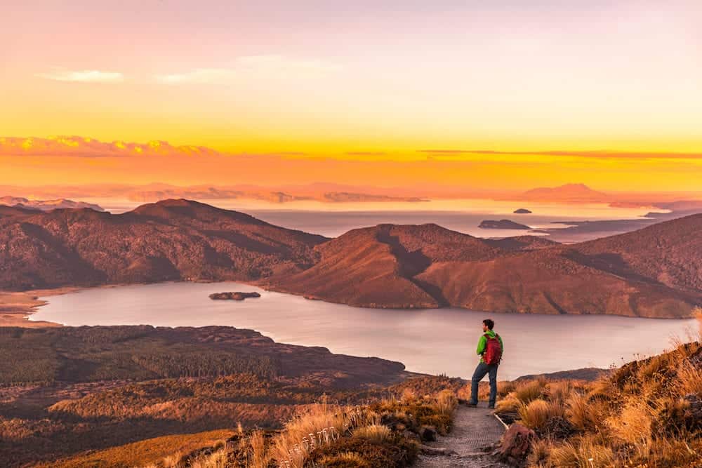 Hiking wanderlust adventure man hiker alone looking at sunset nature landscape of mountains and lakes during summer. Travel outdoors freedom lifestye.