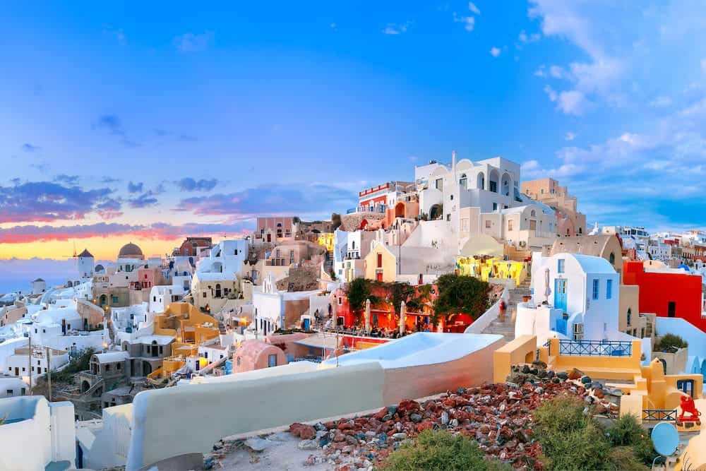 Picturesque panorama, Old Town of Oia or Ia on the island Santorini, white houses, windmills and church with blue domes at sunset, Greece