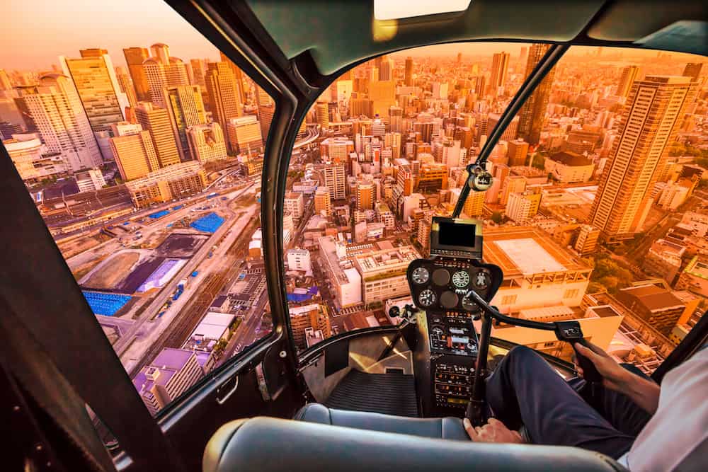 Helicopter cockpit inside the cabin flying on Osaka City Central Business downtown at sunset. Osaka Skyline in Japan. Umeda district aerial view.