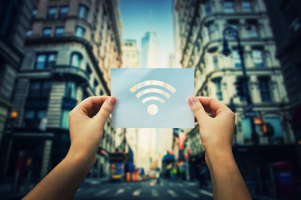 Woman hands holding a paper sheet with WiFi symbol in the middle of the street in a big city. Dreaming of better WiFi, or excellent signal coverage concept. Safe network.