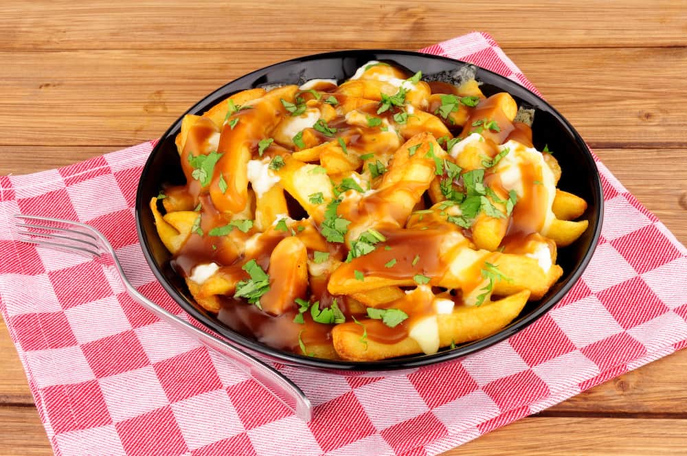 Bowl of traditional Canadian poutine meal on a wooden background