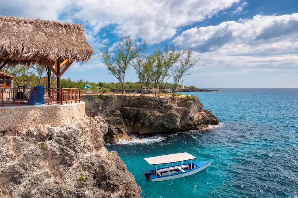 Caribbean rocky beach with turquoise water, tourists boat and lighthouse in Negril Jamaica.