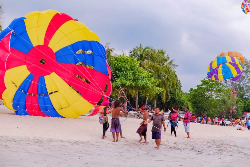 Langkawi, Malaysia - : A group of Malaysian people engaged in parachuting extreme sports on Pantai Tengah Beach, Langkawi island, Malaysia. Summer vacation and fun.