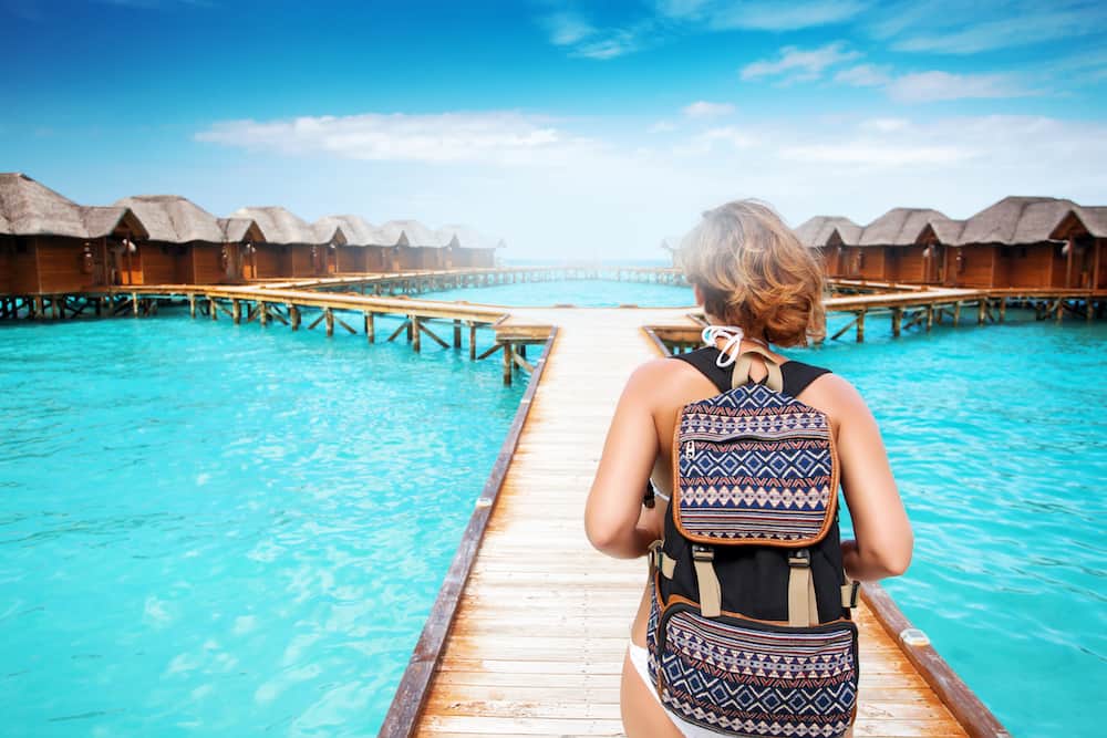 Woman with backpack walk on pier at reopical island resort