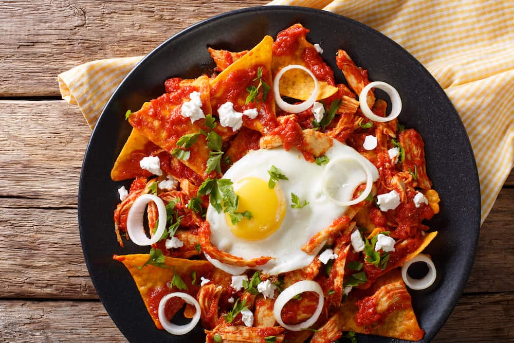 Mexican breakfast: chilaquiles with egg and chicken close-up on a plate. Horizontal view from above