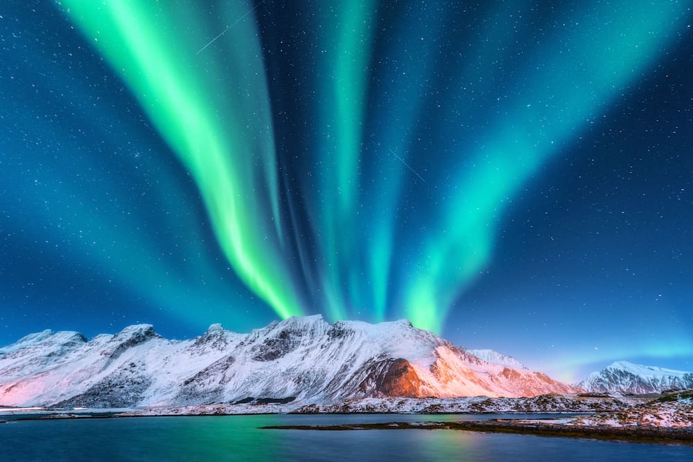 Aurora reflected in water. Northern lights in Lofoten islands, Norway. Blue sky with polar lights. Night landscape with aurora, sea with sky reflection, beach, mountains. Polar lights. Aurora borealis