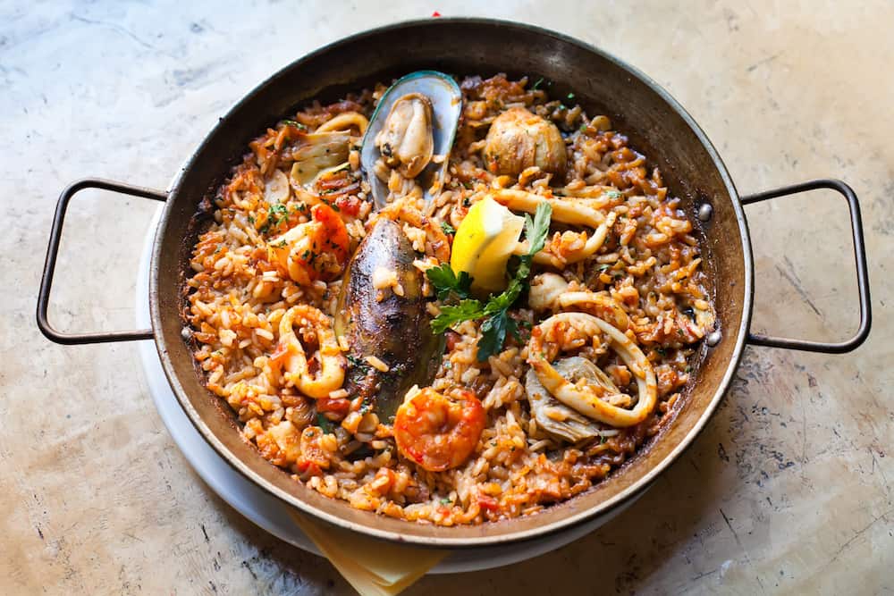 Paella Marinera Traditional, classic spanish main dish paella with shrimp mussels calamares white fish. Aged frying pan with rice, seafood lemon and herbs, up view selective focus