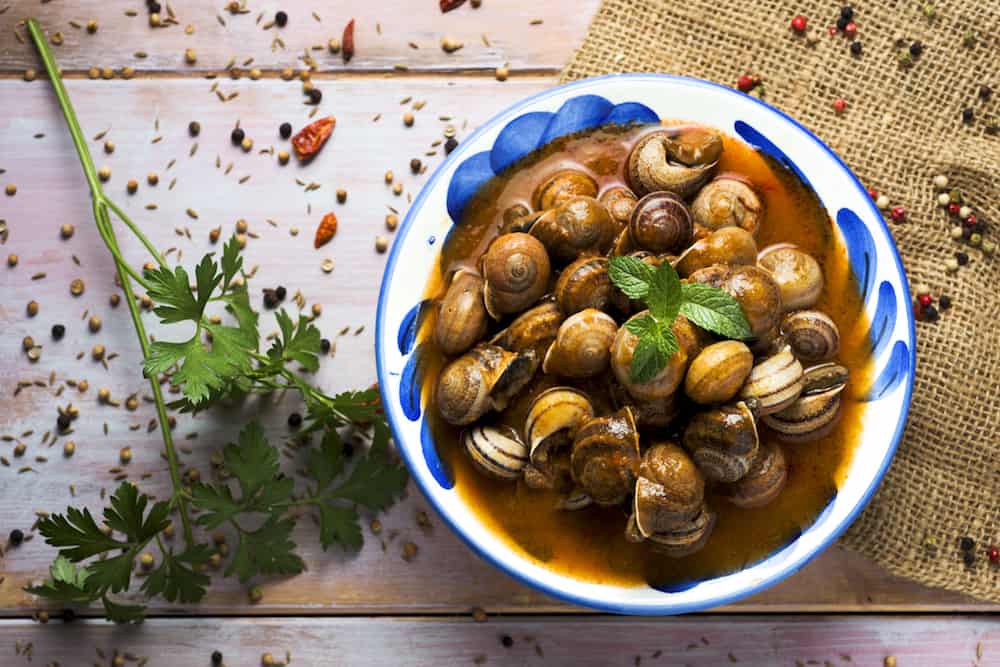 high-angle shot of a ceramic bowl with spanish caracoles en salsa, cooked snails in sauce, on a rustic wooden table