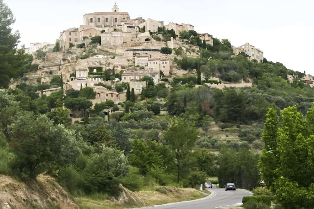 cars driving on road below old hill town of mougins near cannes in southern france