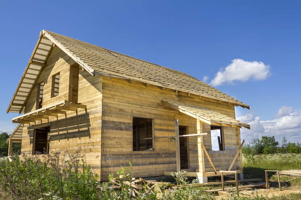 New wooden ecological traditional cottage of natural lumber materials with steep roof under construction in green neighborhood on blue sky copy space background. Professional building concept.