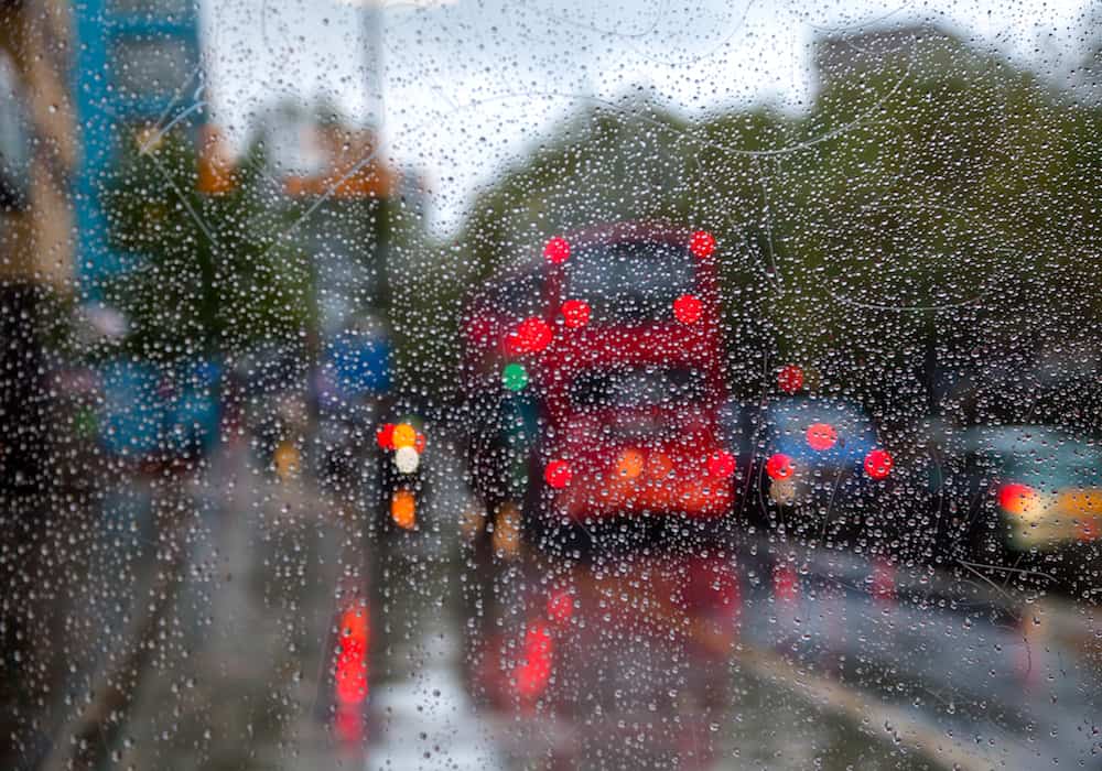 London traffic scene with Doubledecker bus seen through bus stop glass covered with rain drops - autumn rainy weather concept