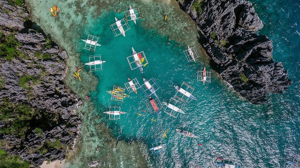 A view from above on a lagoon in which boats brought tourists for a rest. Aerial view of the turquoise water between the black steep cliffs.