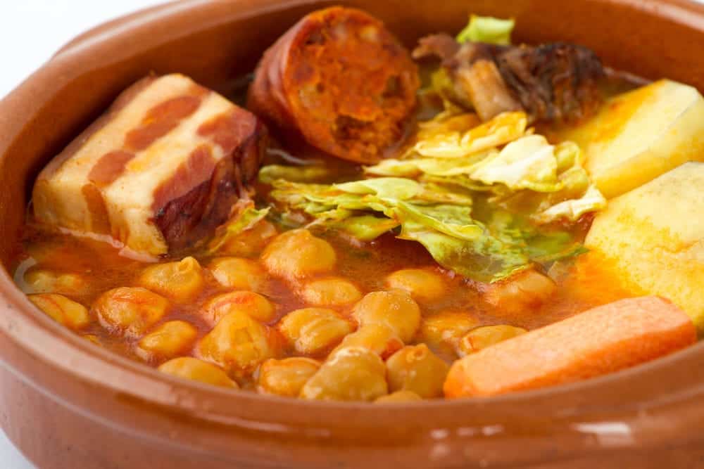 Cocido de Madrid, traditional Spanish dish with chickpeas. meat, sasuages, and vegetables, in a typical dish, isolated on white