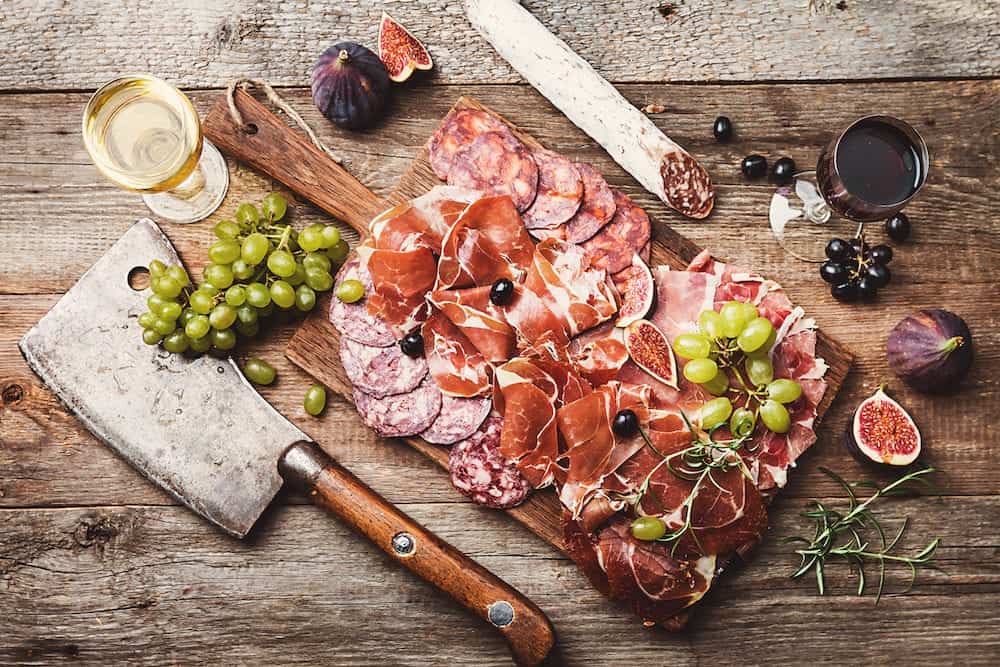 Sliced jamon on cutting board with figs, grapes and red wine. Parma ham, hamon on wooden background with copy space, top view. Jamon Serrano, Iberico. Traditional Spanish ham