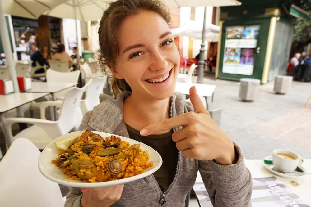 Paella - Spanish local food. Smiling woman points a finger at a plate of paella at outdoor restaurant. Travel in Spain.
