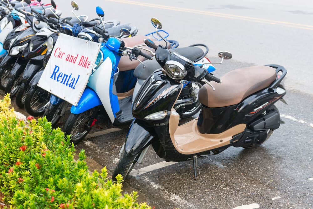 AO NANG KRABI THAILAND - : Row of motorbikes for rent to tourists for transportation parked on an urban road with advertising