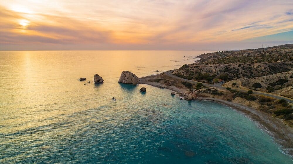 Aerial Bird's eye view of Petra tou Romiou, aka Aphrodite's rock a famous tourist travel destination landmark in Paphos, Cyprus. The sea bay of goddess Afroditi birthplace at sunset from above.