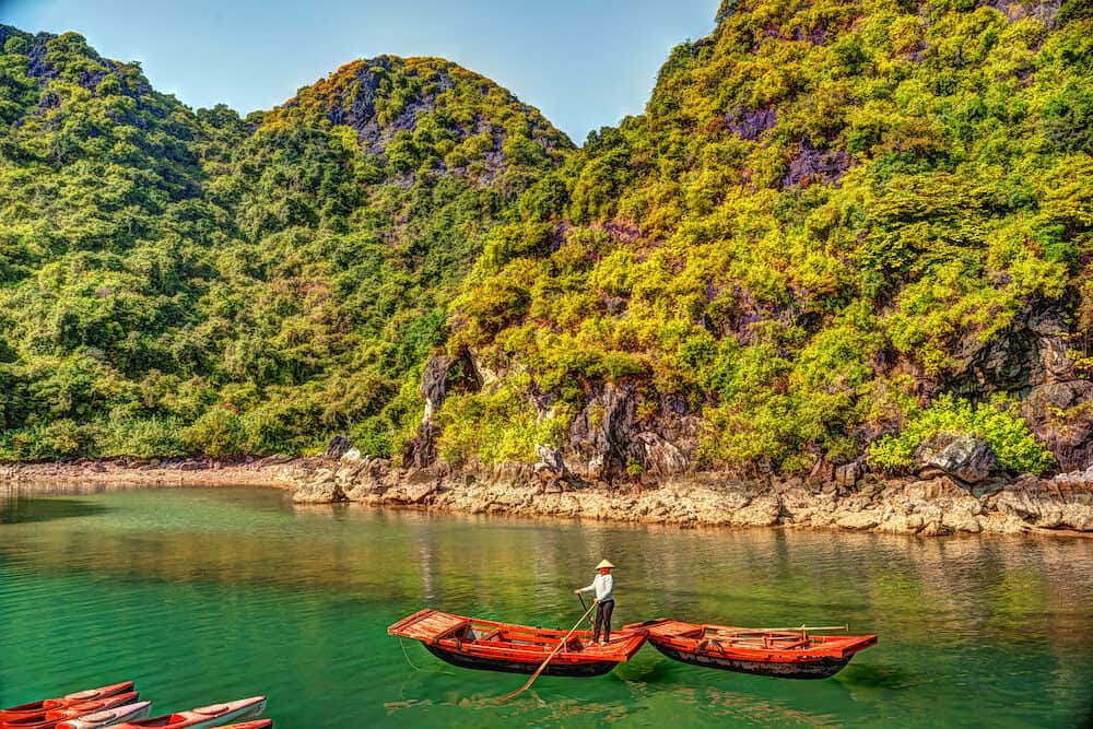 Unrecognizable vietnamese woman rowing boats that bring tourists traveling inside limestone cave with limestone island in background in summer at Halong Bay. Vietnam.