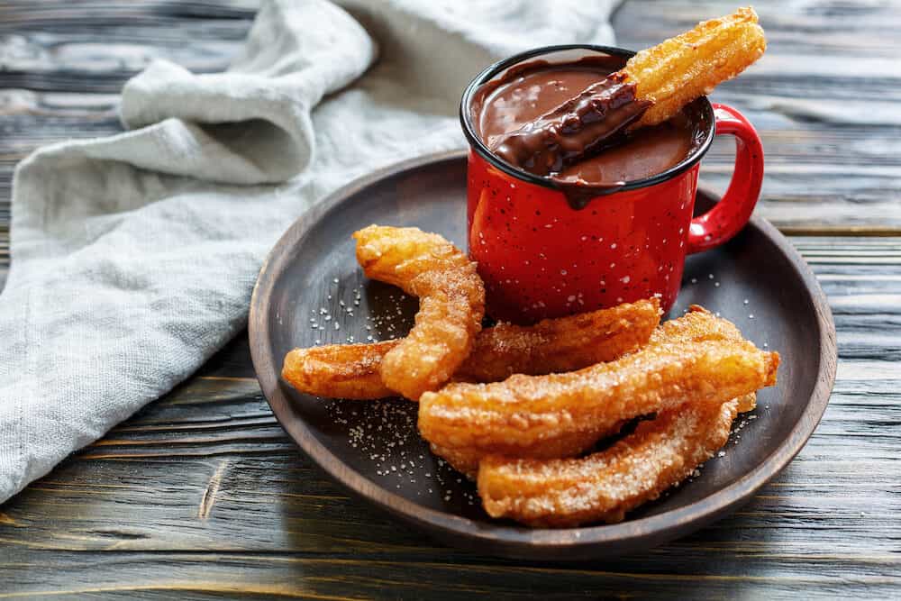 Dish served with a traditional Spanish dessert churros and hot chocolate on wooden table. Selective focus.