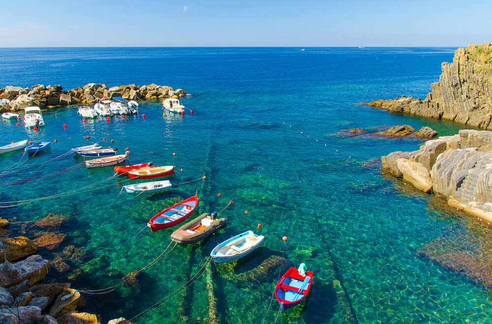 Fishing colorful boats on transparent water in small harbor of Riomaggiore village National park Cinque Terre, Ligurian and Mediterranean Sea, coastline of Riviera di Levante, Liguria, Italy