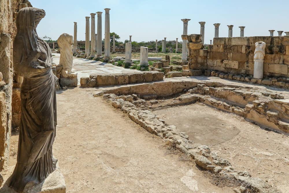 Famagusta, Turkish Republic of Northern Cyprus. Corinthian columns and sculptures at bath complex in ancient city Salamis ruins. Sunny day, blue sky.