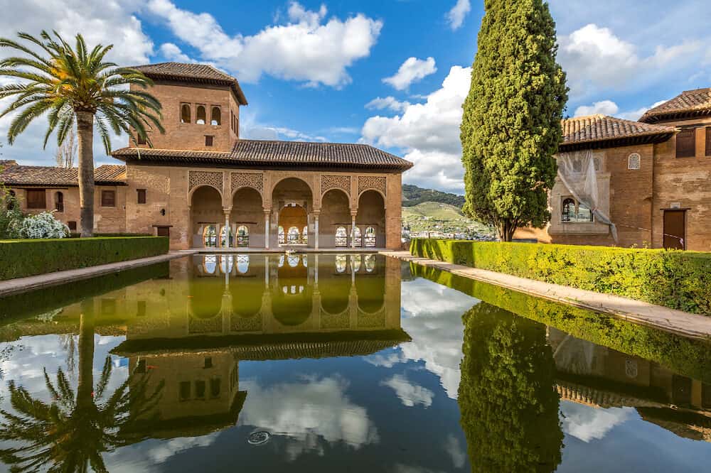 El Partal in Alhambra of Granada, Unesco Heritage Site, Andalusia, Spain. A large central pond faces the arched portico which stands behind the Tower of the Ladies reflecting in the water.