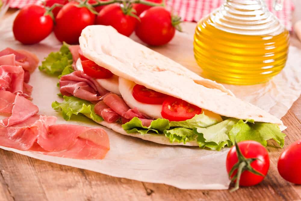 Piadina with ham and lettuce on wooden table.
