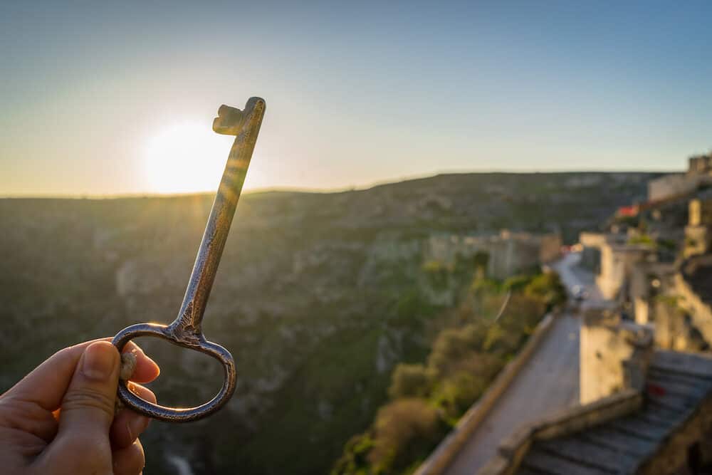 travel concept with closed up of woman hand holding a vintage hotel key morning sunrise in Matera Italy