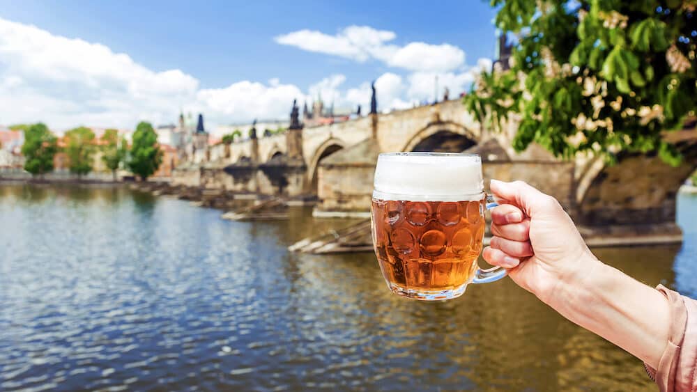 hand with a mug of the Czech beer against the background of Charles bridge in Prague