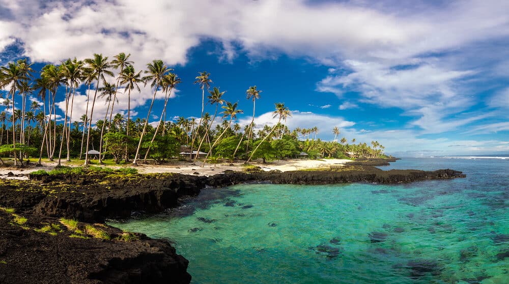Beach with coral reef on south side of Upolu framed by palm leaves, Samoa Islands