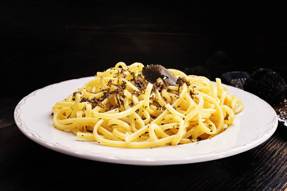 Strangozzi, italian wheat pasta with black truffle on a black wooden board.