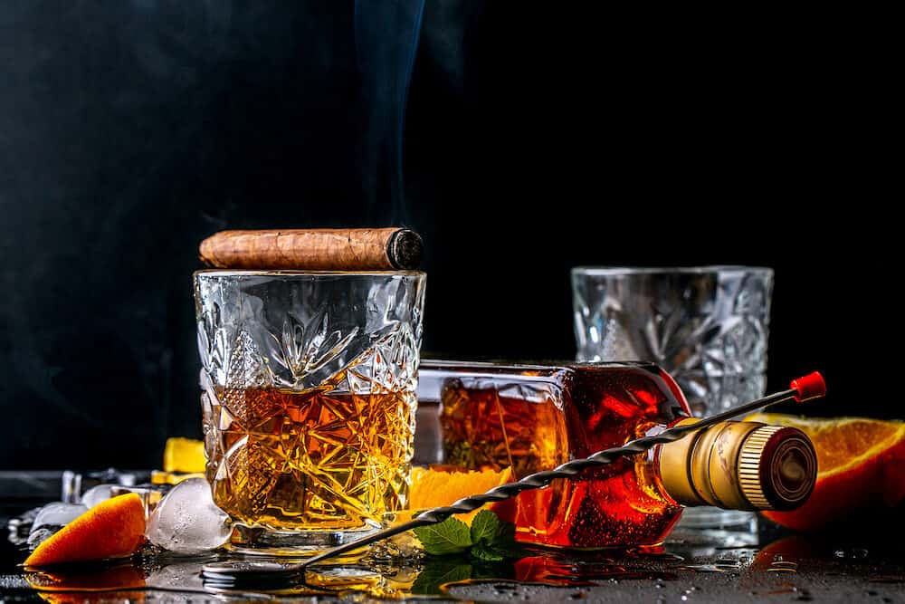 Elite drink for masculine relaxation Two glasses of whiskey, rum and smoking cigar, ice on black background, copy space. concept luxury drink.