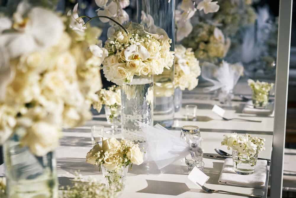 The wedding reception dinner venue setup with the white flower theme, A bunch of white roses, flower, floral decoration on the dinner table.