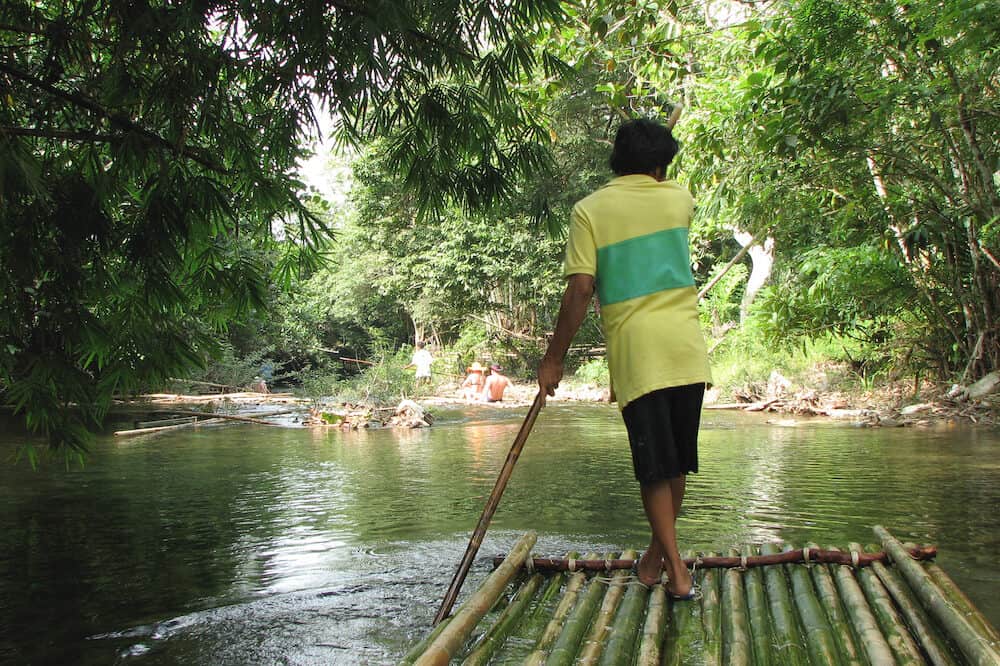 Adventure rafting on bamboo rafts on a mountain jungle river in Khao Lak Park, Thailand. Man controls the raft with a long pole, rear view.