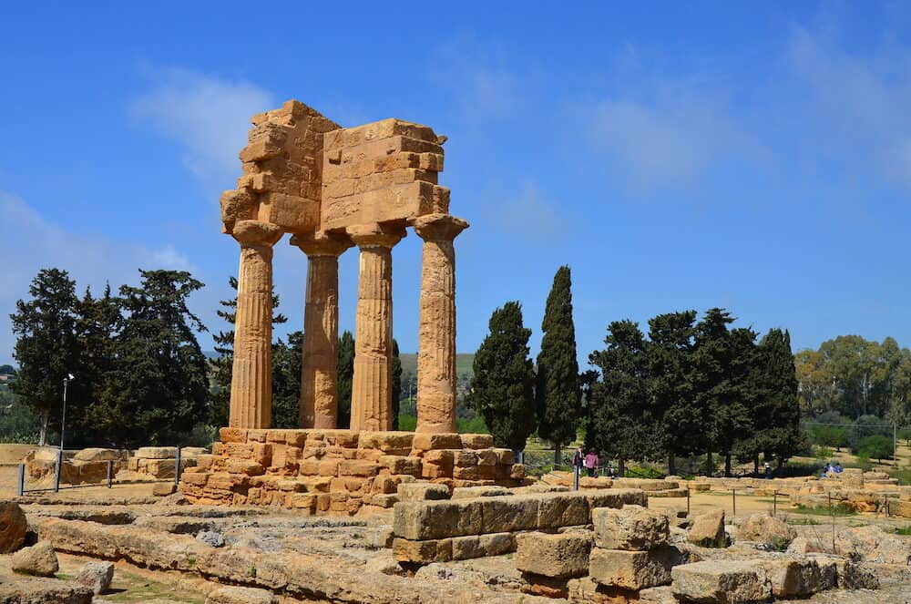 Temple of Dioscuri (Castor and Pollux) with Agrigento town in the Background. Famous ancient ruins in Valley of Temples, Agrigento, Sicily, Italy. UNESCO World Heritage Site.