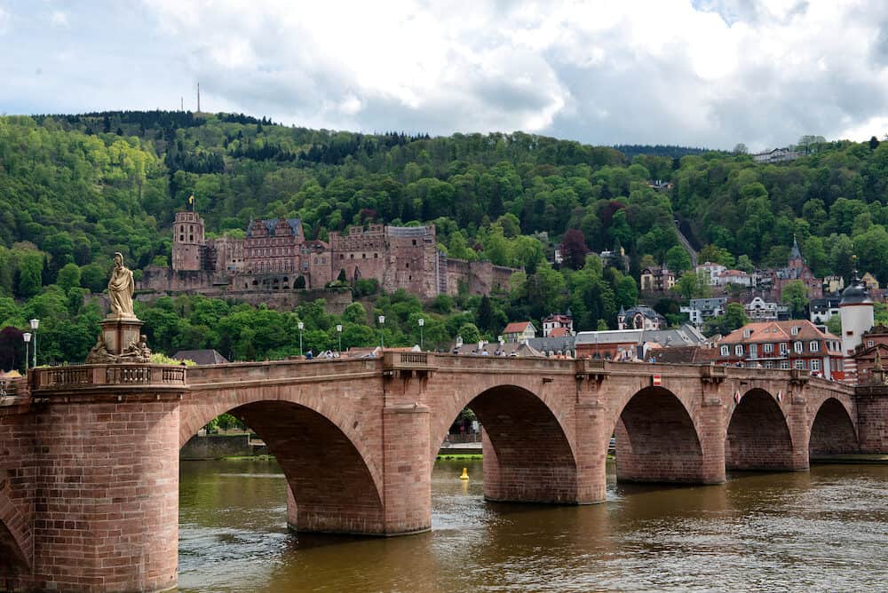 Historic Neuenheim Old Bridge in Heidelberg, Germany crossing the Neckar River with the ruins of the Heidelberg castle on the hillside overlooking the town