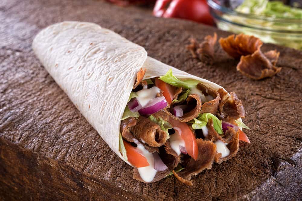A delicious doner donair kebab wrap with spicy meat, lettuce, tomato, red onion and sauce.