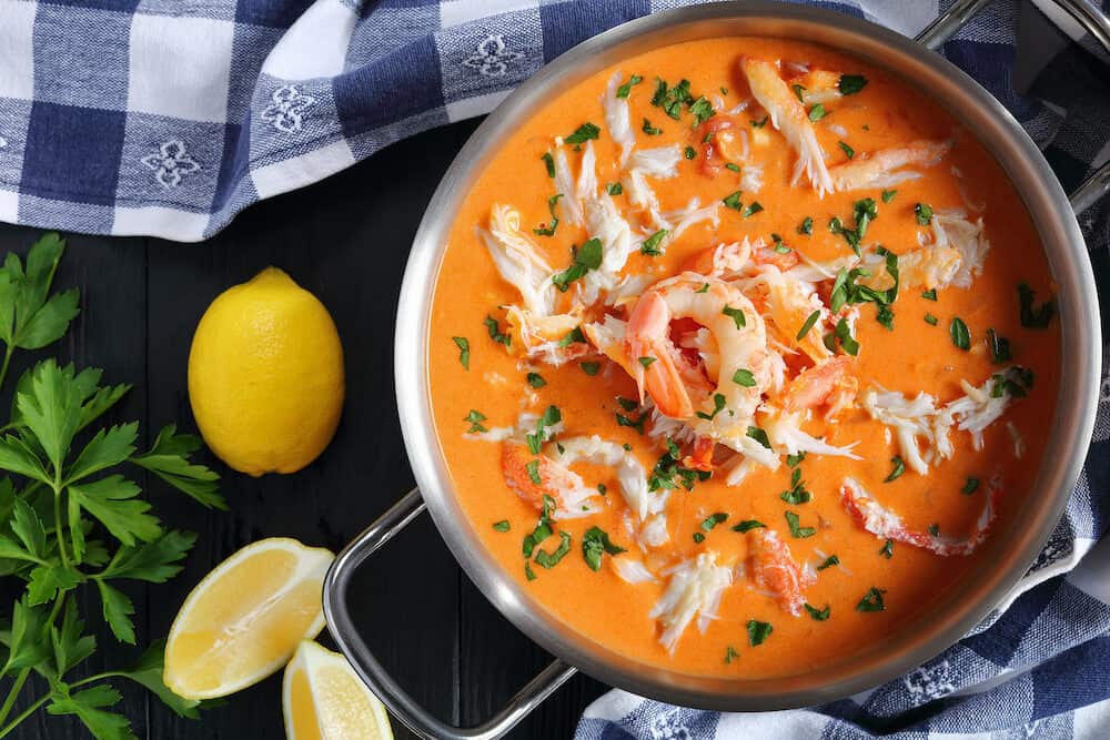 savory delicious hot bisque or thick soup of shredded snow crab meat, prawn, lobster in a stainless metal casserole on black wooden table, authentic french recipe, vertical view from above