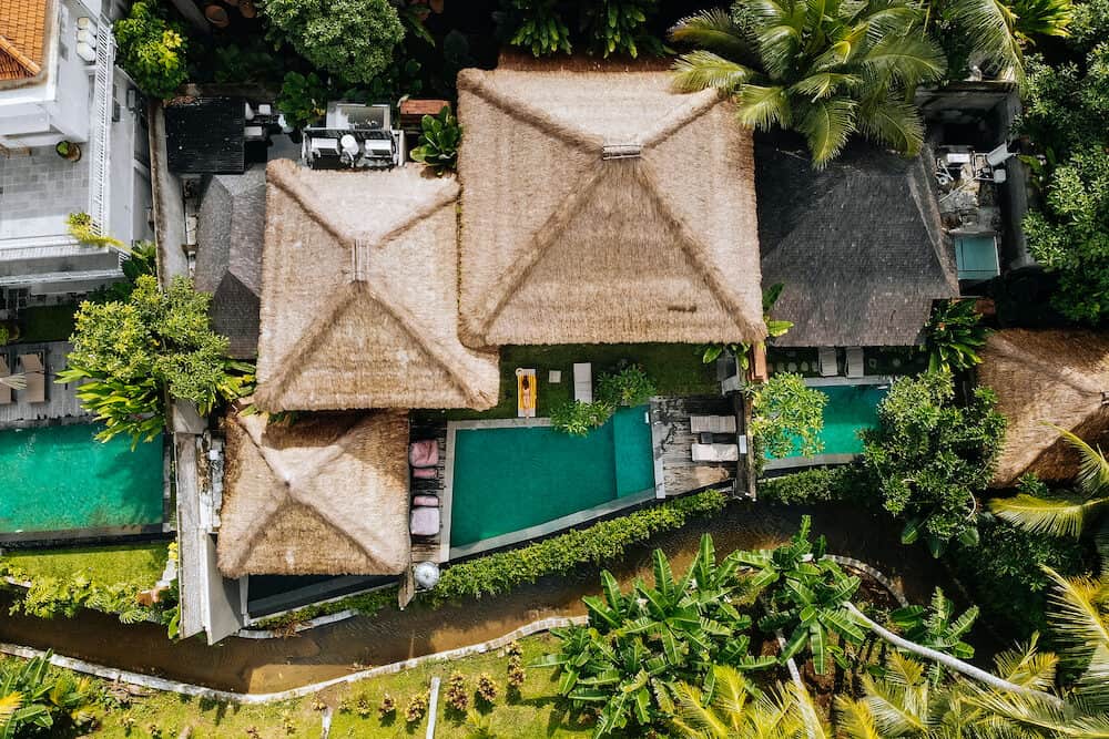 Top drone view of luxury hotel with straw roof villas and pools in tropical jungle and palm trees. Luxurious villa, pavilion in forest, Ubud, Bali