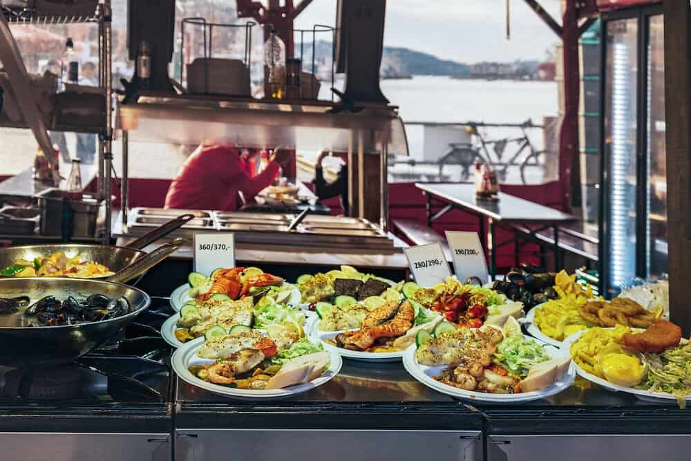 Delicious plates with a variety of grilled fish and seafood served with salad, french Fries and mayonnaise sauce. Street Food ready to eat with price tag at Bergen Fish Market, Norway