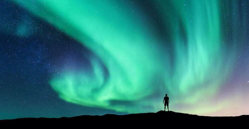 Aurora borealis and silhouette of standing man. Lofoten islands, Norway. Aurora and happy man. Sky with stars and green polar lights. Night landscape with aurora and people. Concept. Nature background