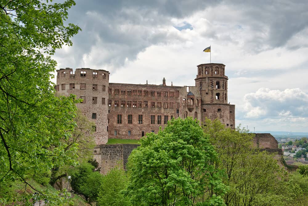Green vegetation in front of the ruins of Heidelberg Castle, historical tourist attraction, under a dramatic cloudy sky, in Germany