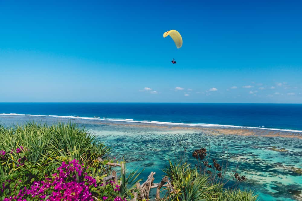 Shore and blue ocean with paraglider in tropical island.