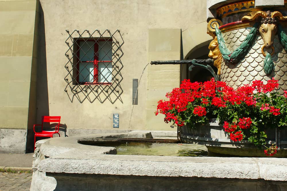 Fountain with water and red flowers at the ancient square Münsterplatz near the cathedral in Bern, Switzerland, during summer