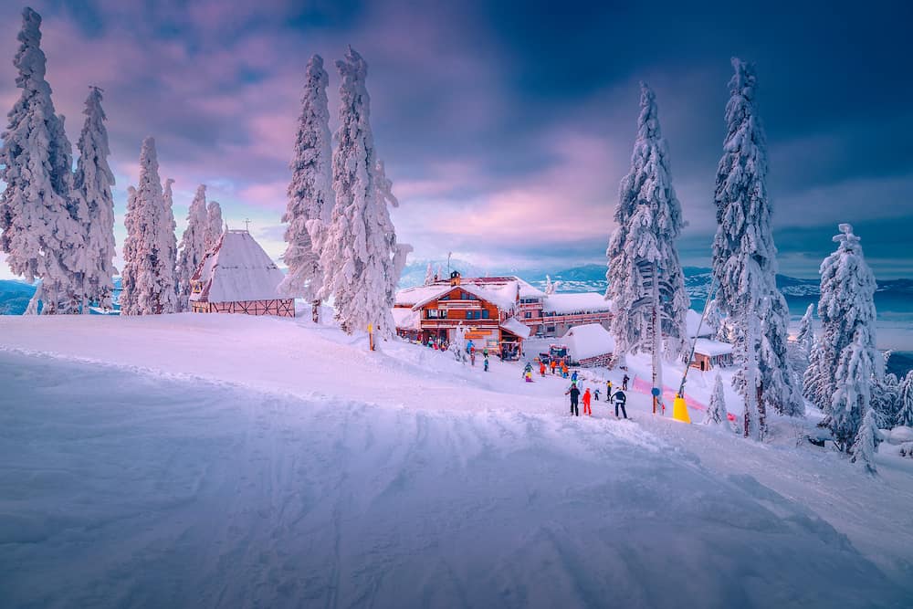 Spectacular winter ski resort with skiers in Romania. Fantastic touristic and winter sport holiday location. Beautiful sunset in Poiana Brasov ski resort, Transylvania, Romania, Europe