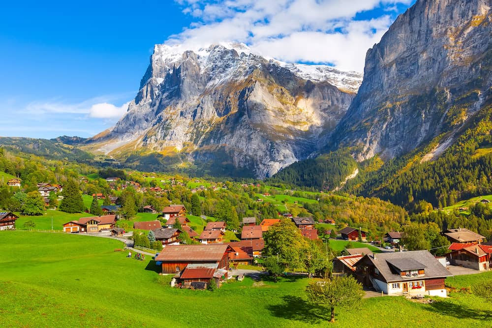 Grindelwald, Switzerland aerial village view and autumn Swiss Alps mountains panorama landscape, wooden chalets on green fields and high peaks in background, Bernese Oberland, Europe