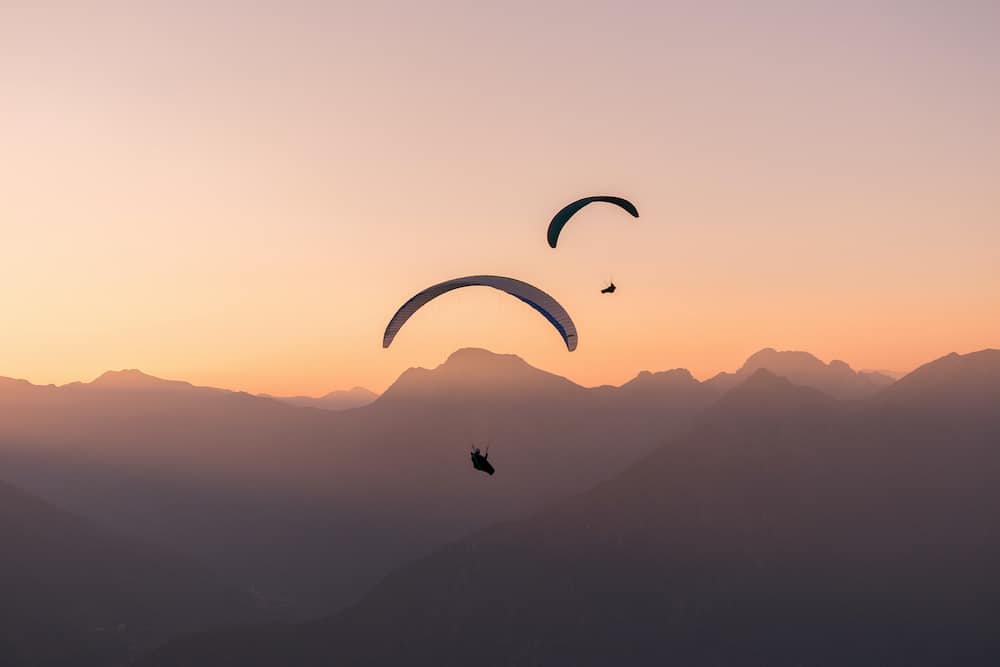 Paragliding over the Swiss Alps. Silhouettes of paragliders in the pink light of sunset.